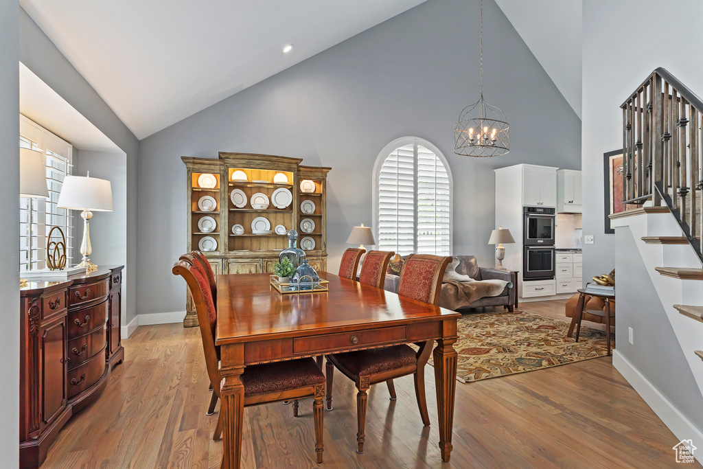 Dining room featuring high vaulted ceiling, stairway, a chandelier, and light wood-style floors