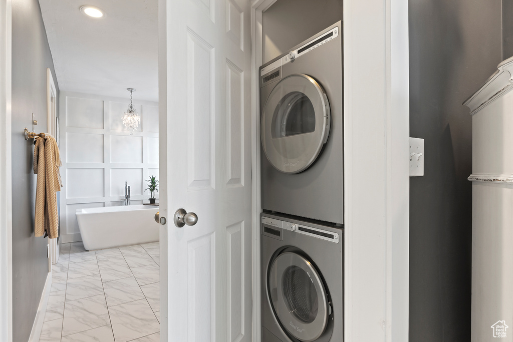 Washroom with a chandelier, recessed lighting, stacked washer / drying machine, and marble finish floor