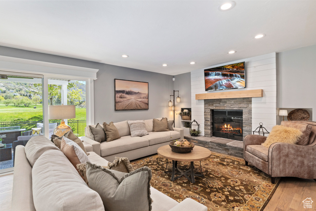 Living room with wood finished floors, recessed lighting, and a stone fireplace