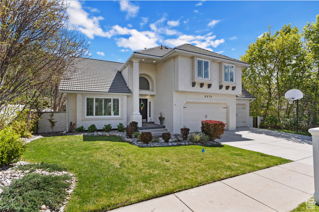 Traditional-style house featuring a front yard, a garage, a tiled roof, brick siding, and concrete driveway