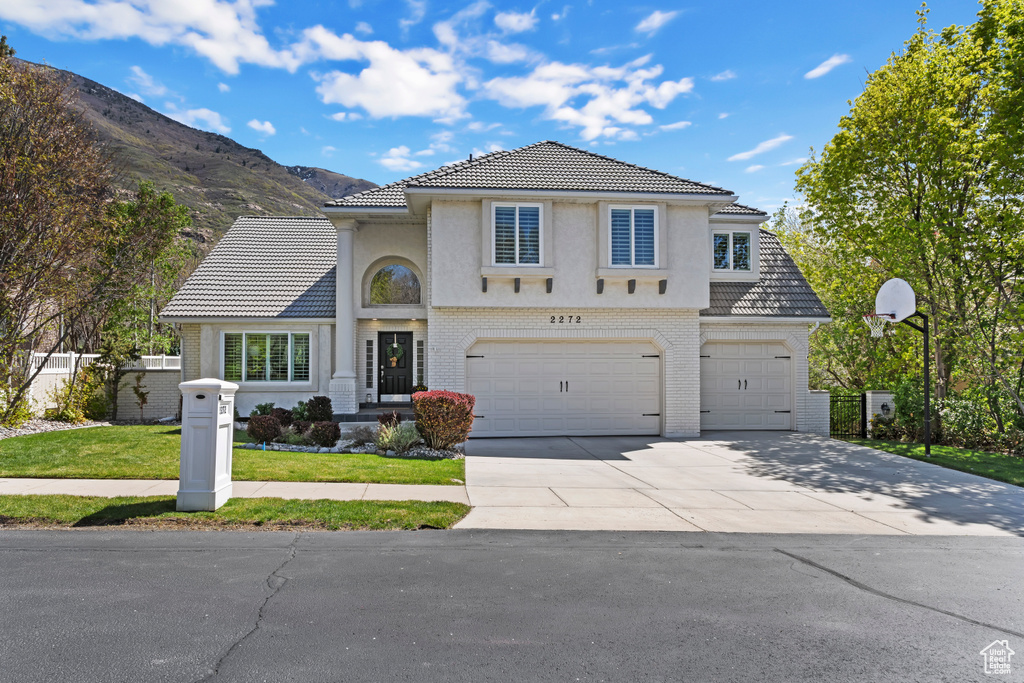 Traditional-style home with a tile roof, a mountain view, brick siding, concrete driveway, and an attached garage
