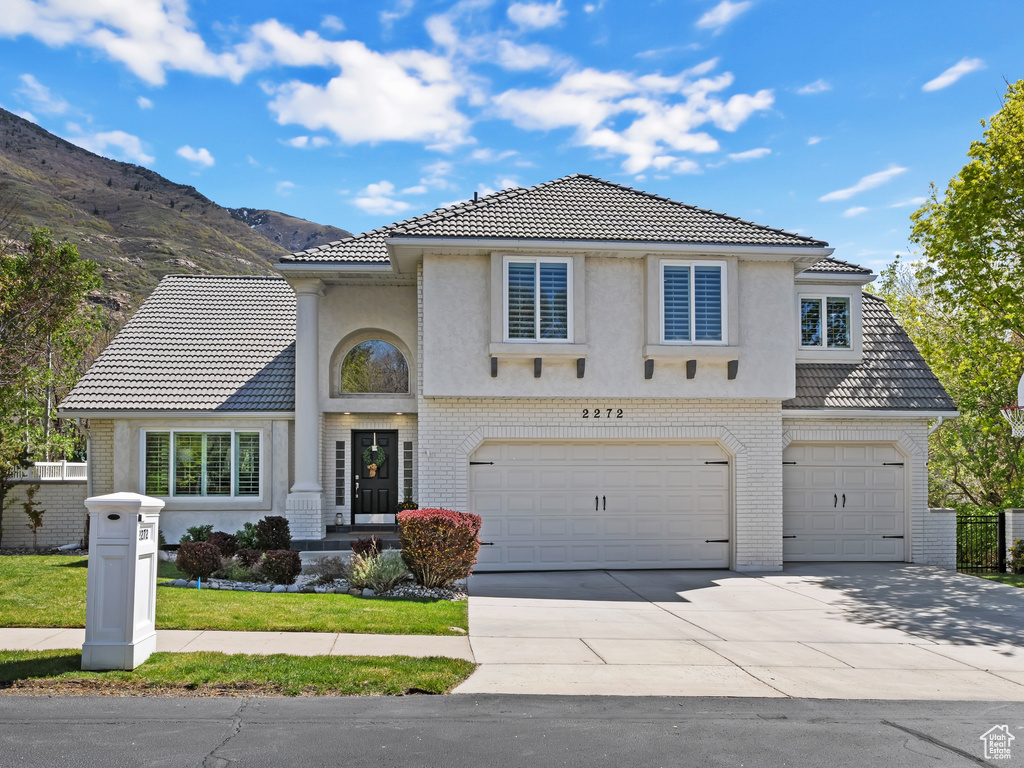 View of front of house with brick siding, concrete driveway, a garage, a tile roof, and a mountain view