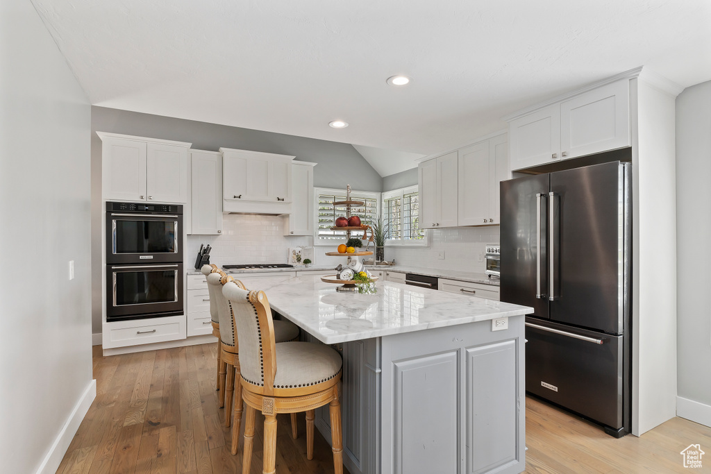 Kitchen with vaulted ceiling, high end refrigerator, white cabinetry, a center island, and multiple ovens