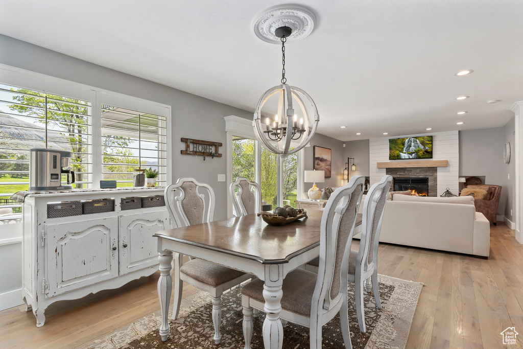 Dining space with light wood finished floors, recessed lighting, a notable chandelier, and a warm lit fireplace