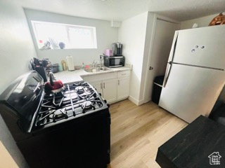Kitchen featuring stainless steel microwave, white cabinets, freestanding refrigerator, black range with gas stovetop, and light wood finished floors