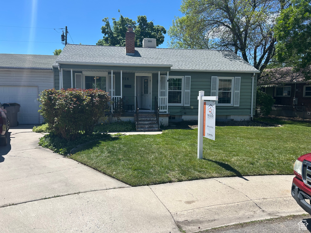 Single story home featuring a chimney, covered porch, an attached garage, a shingled roof, and a front yard