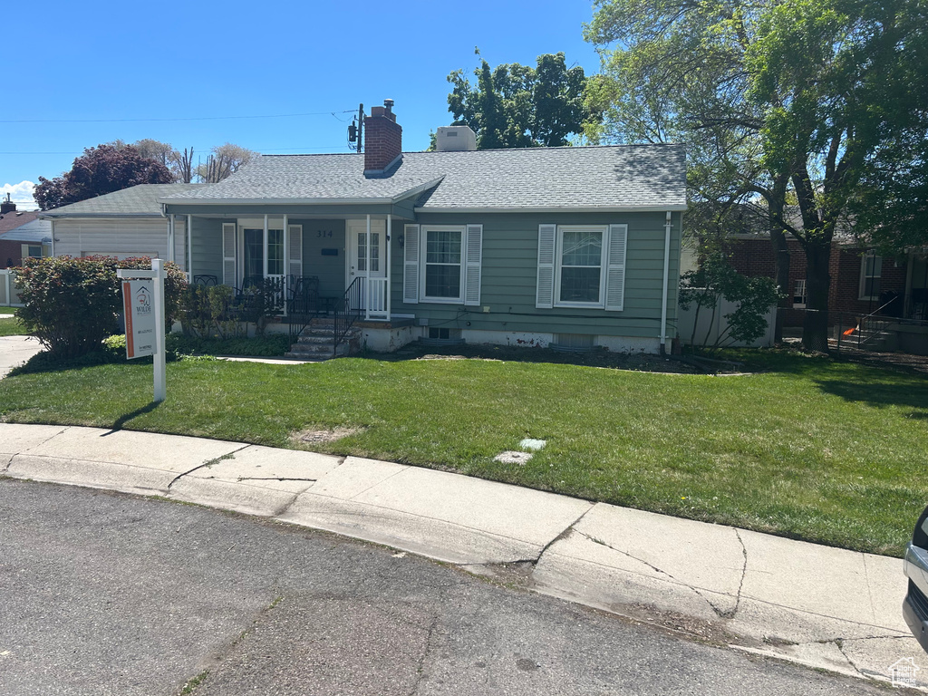 Ranch-style house with covered porch, roof with shingles, a chimney, and a front yard