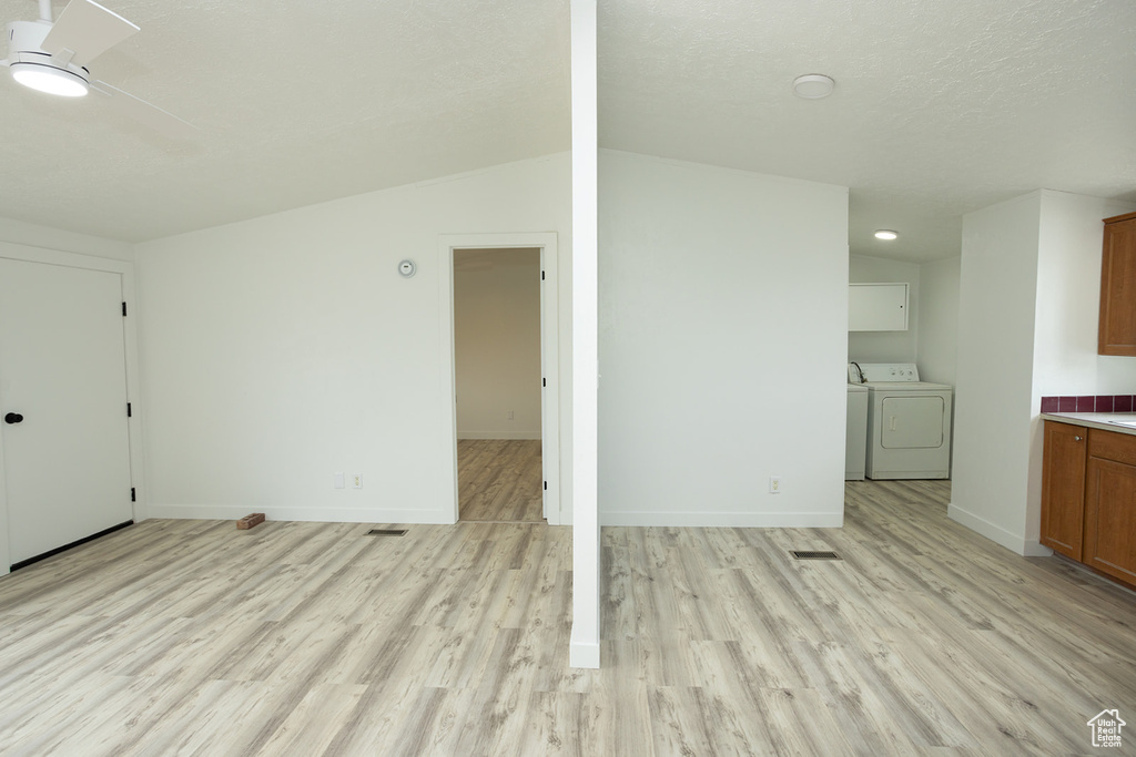 Unfurnished living room with a ceiling fan, baseboards, washer and clothes dryer, and light wood-style flooring