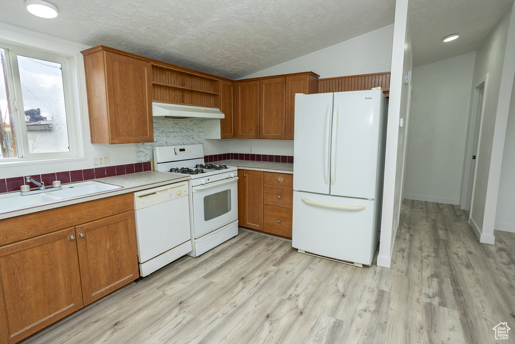 Kitchen featuring a sink, light countertops, light wood finished floors, under cabinet range hood, and white appliances