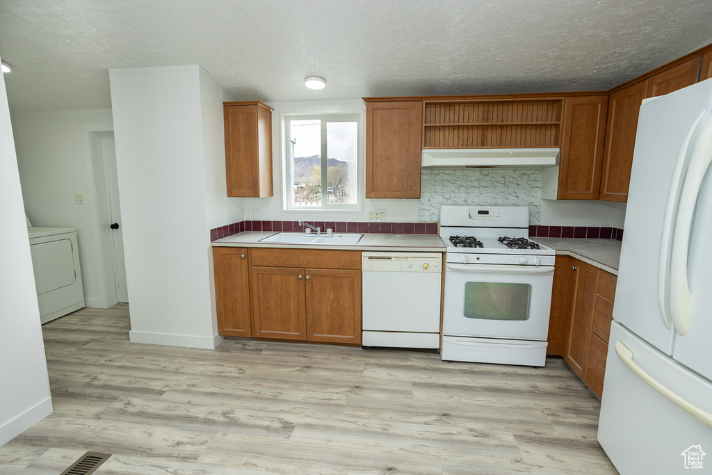Kitchen with brown cabinets, a sink, white appliances, washer / clothes dryer, and under cabinet range hood