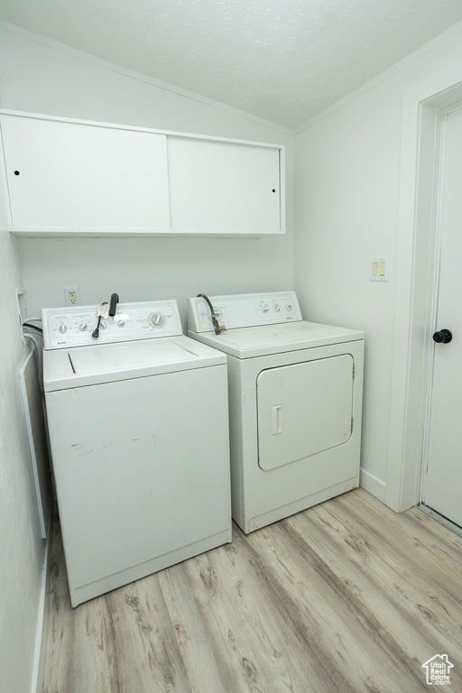 Clothes washing area with light wood finished floors and washer and clothes dryer