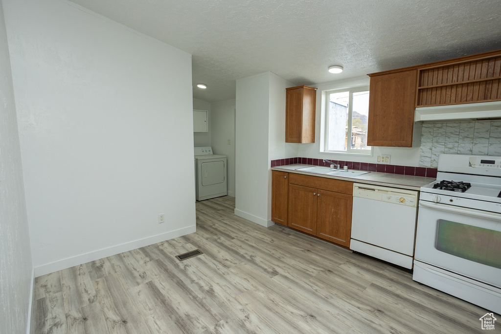 Kitchen with white appliances, washer / clothes dryer, light wood-type flooring, under cabinet range hood, and a sink