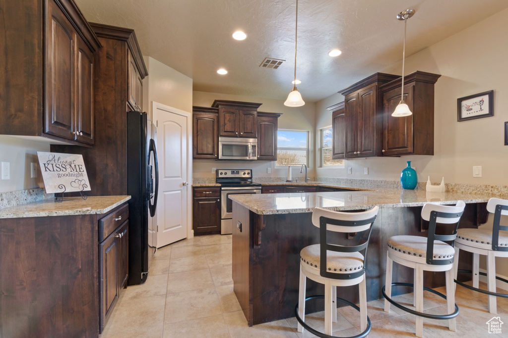 Kitchen featuring hanging light fixtures, appliances with stainless steel finishes, light stone counters, light tile floors, and sink
