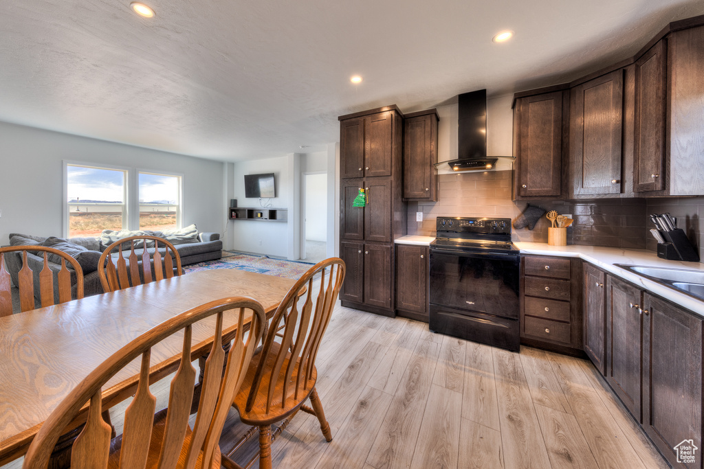 Kitchen with wall chimney exhaust hood, dark brown cabinetry, black electric range, decorative backsplash, and light countertops