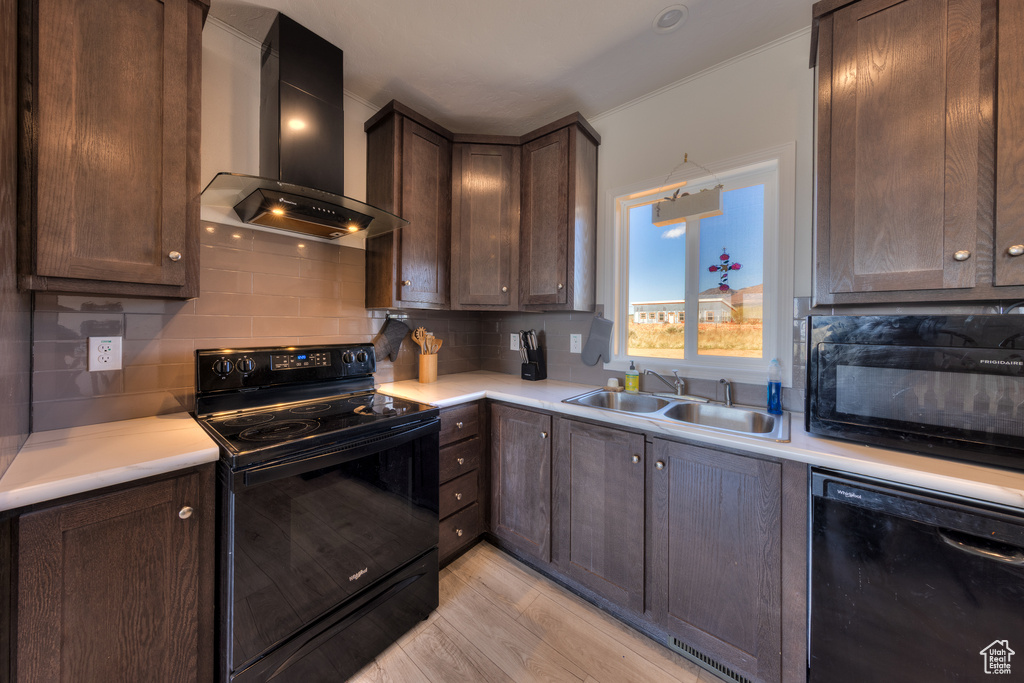 Kitchen featuring light countertops, a sink, wall chimney exhaust hood, black appliances, and tasteful backsplash