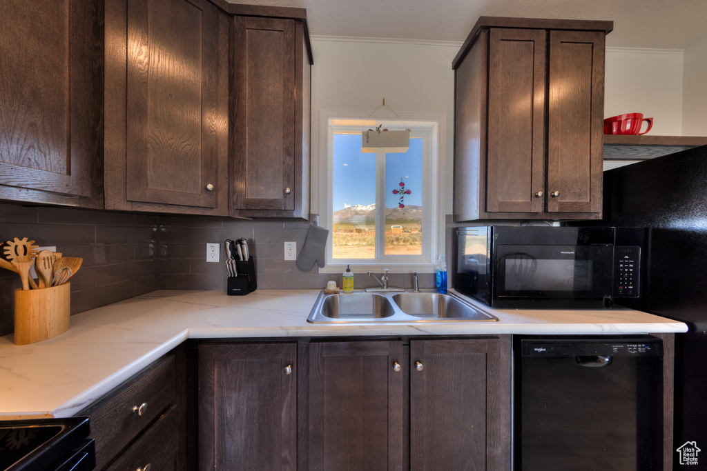 Kitchen featuring black appliances, decorative backsplash, dark brown cabinets, and a sink