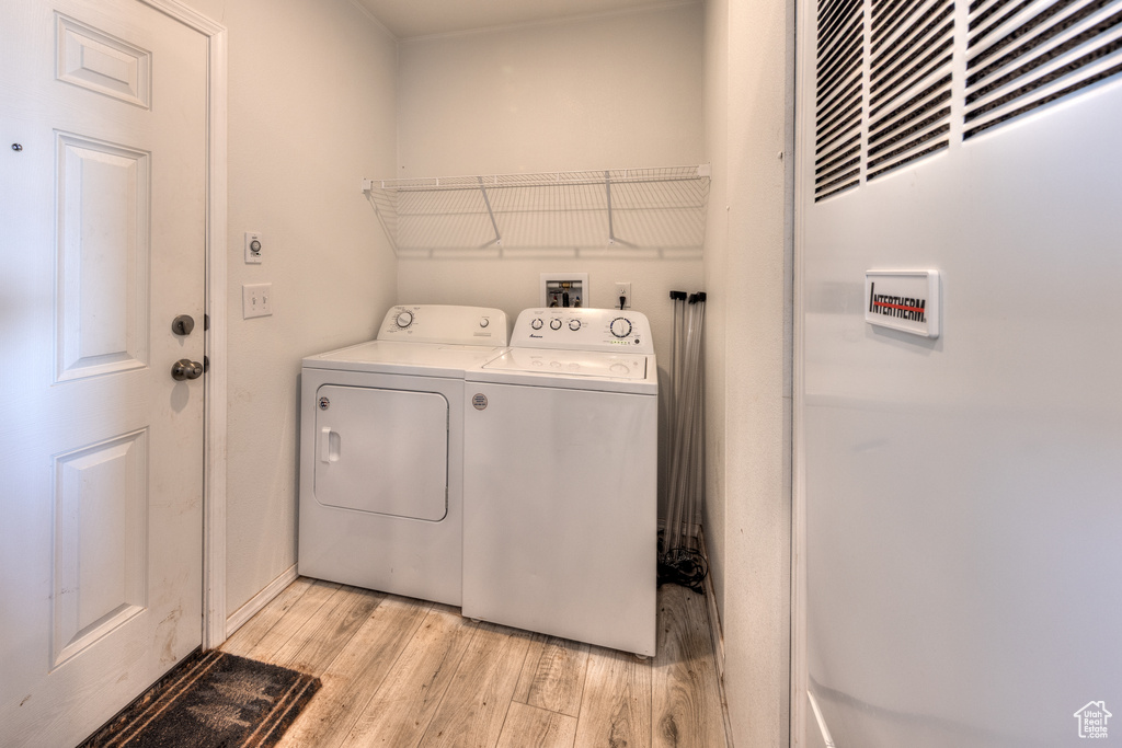 Washroom with a heating unit, washer and clothes dryer, laundry area, and light wood-style flooring