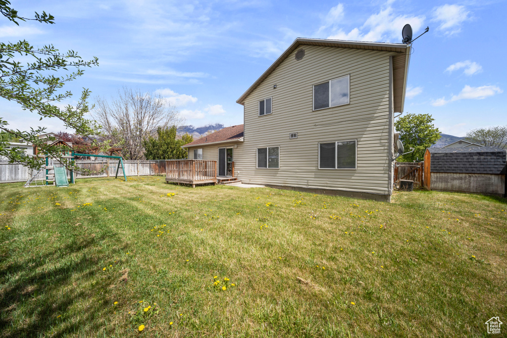 Rear view of house featuring a fenced backyard, a playground, a wooden deck, and a yard