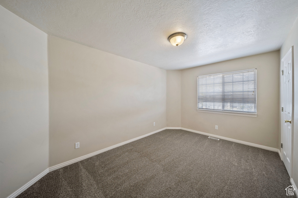 Unfurnished room featuring baseboards, dark colored carpet, a textured ceiling, and visible vents