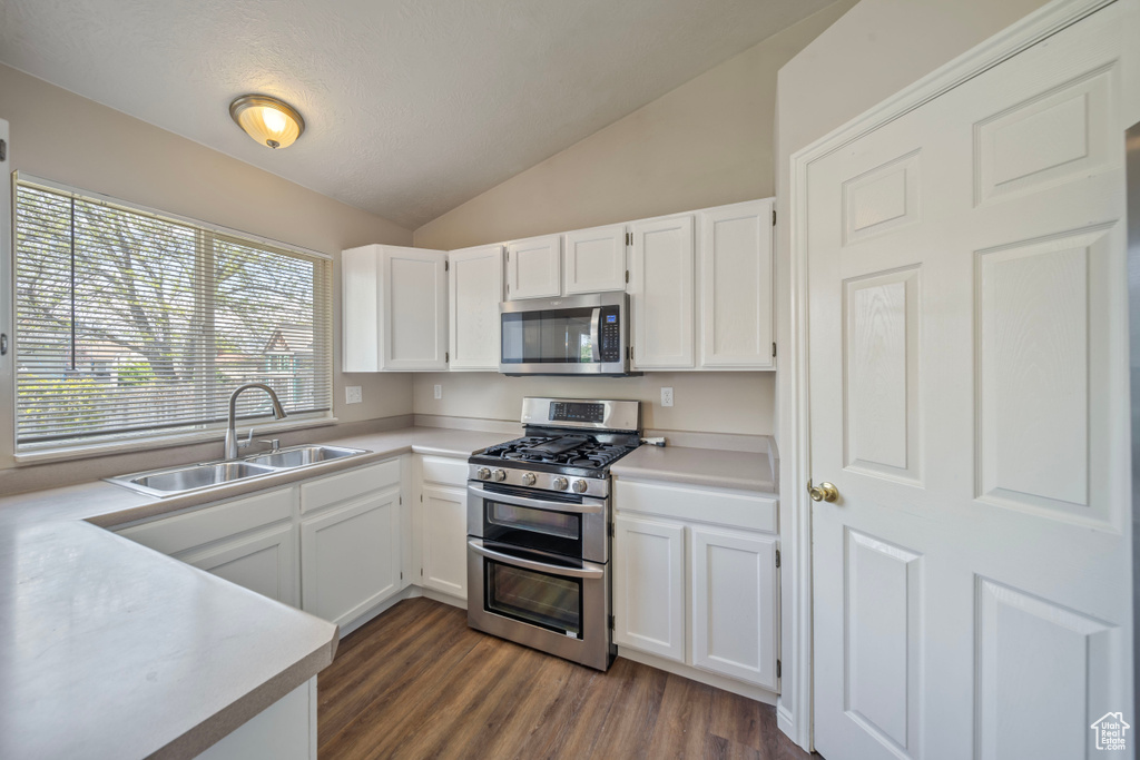 Kitchen featuring white cabinets, dark wood-style flooring, appliances with stainless steel finishes, a sink, and lofted ceiling