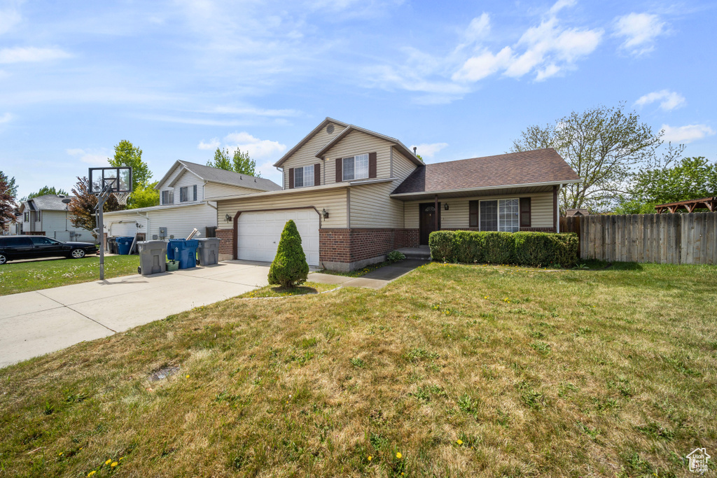View of front of house featuring fence, a front yard, brick siding, concrete driveway, and an attached garage