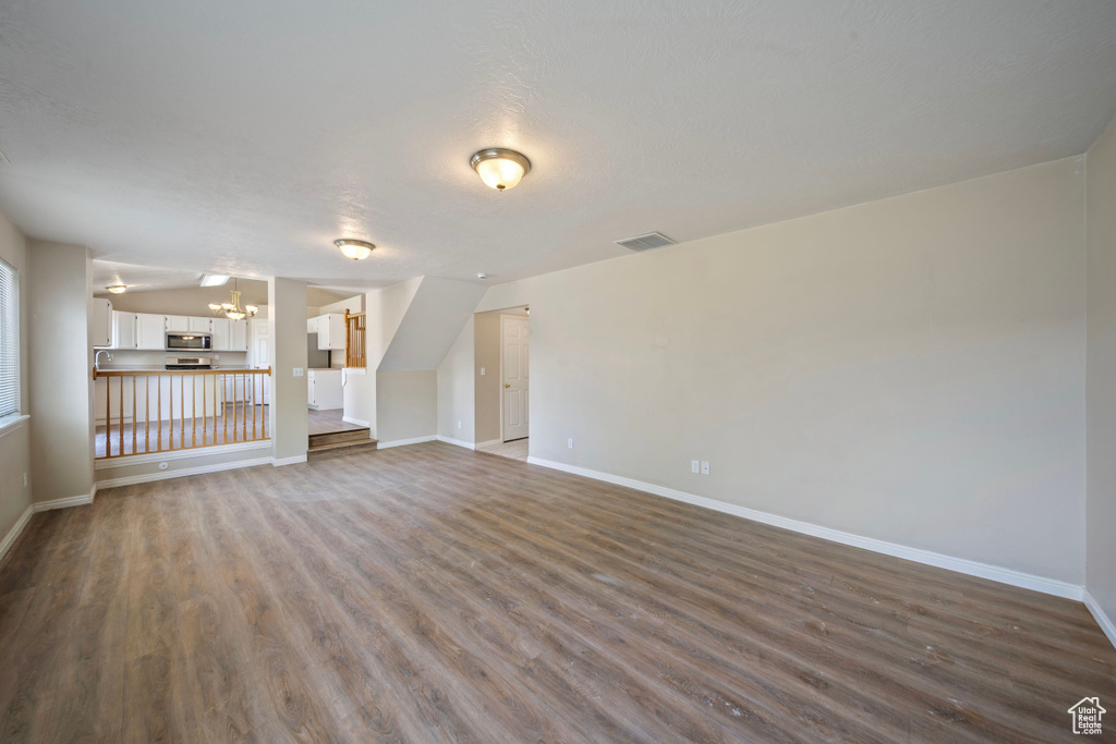 Unfurnished living room featuring baseboards, a chandelier, visible vents, and dark wood-type flooring