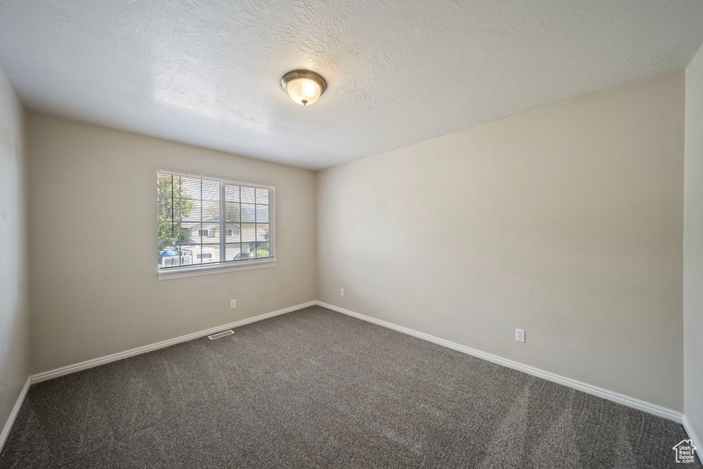 Spare room featuring dark colored carpet, a textured ceiling, and baseboards