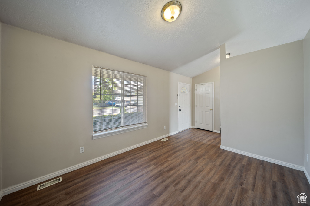 Unfurnished room featuring baseboards, lofted ceiling, dark wood-style floors, and visible vents