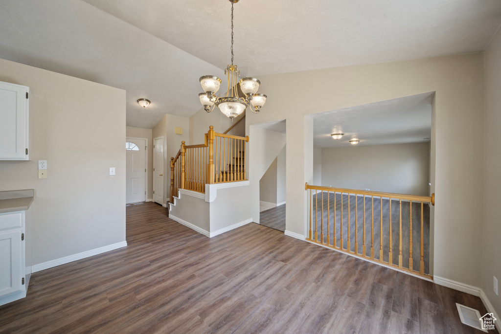 Unfurnished dining area featuring a notable chandelier, baseboards, dark wood finished floors, and visible vents