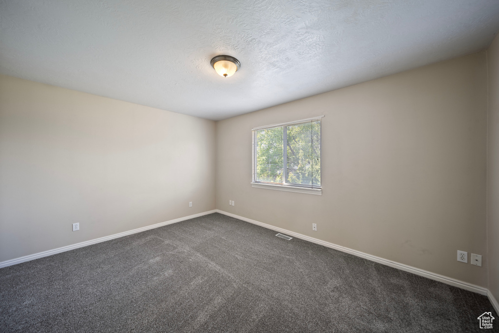 Spare room with a textured ceiling, baseboards, visible vents, and dark colored carpet