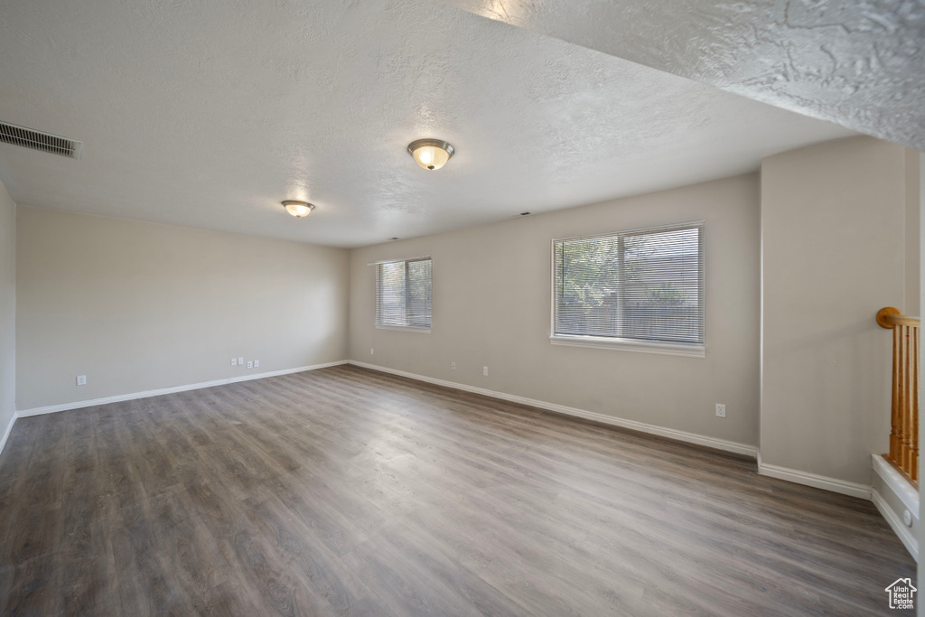 Empty room with baseboards, a textured ceiling, visible vents, and dark wood finished floors