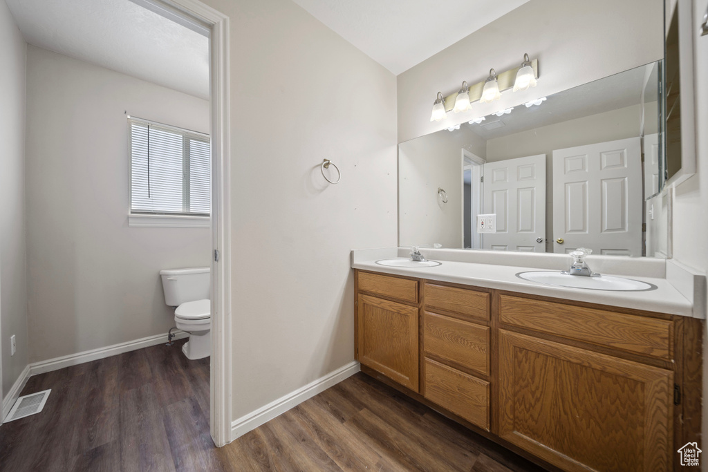 Bathroom with a sink, double vanity, toilet, wood finished floors, and visible vents
