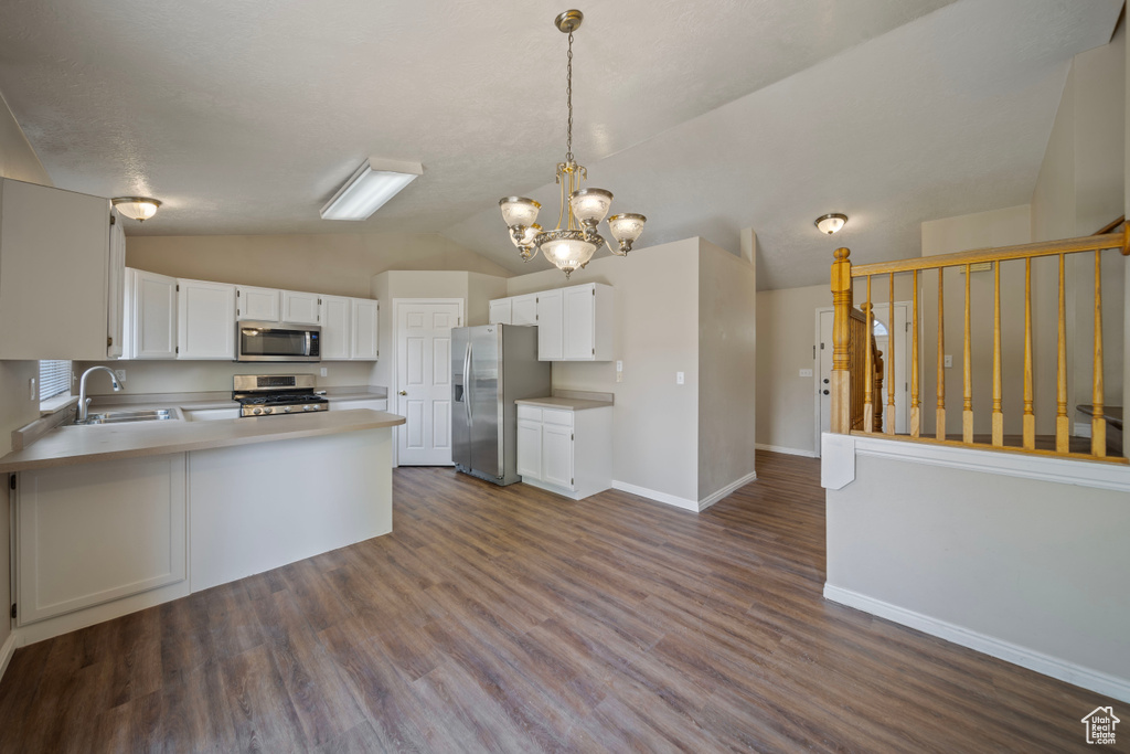 Kitchen with an inviting chandelier, lofted ceiling, baseboards, light countertops, and appliances with stainless steel finishes