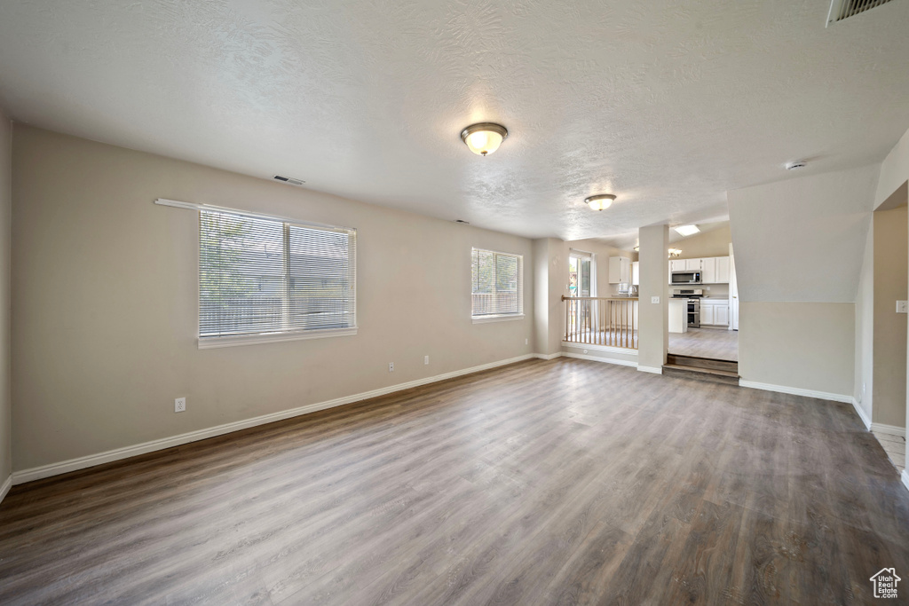 Unfurnished living room with baseboards, dark wood-style flooring, and a textured ceiling