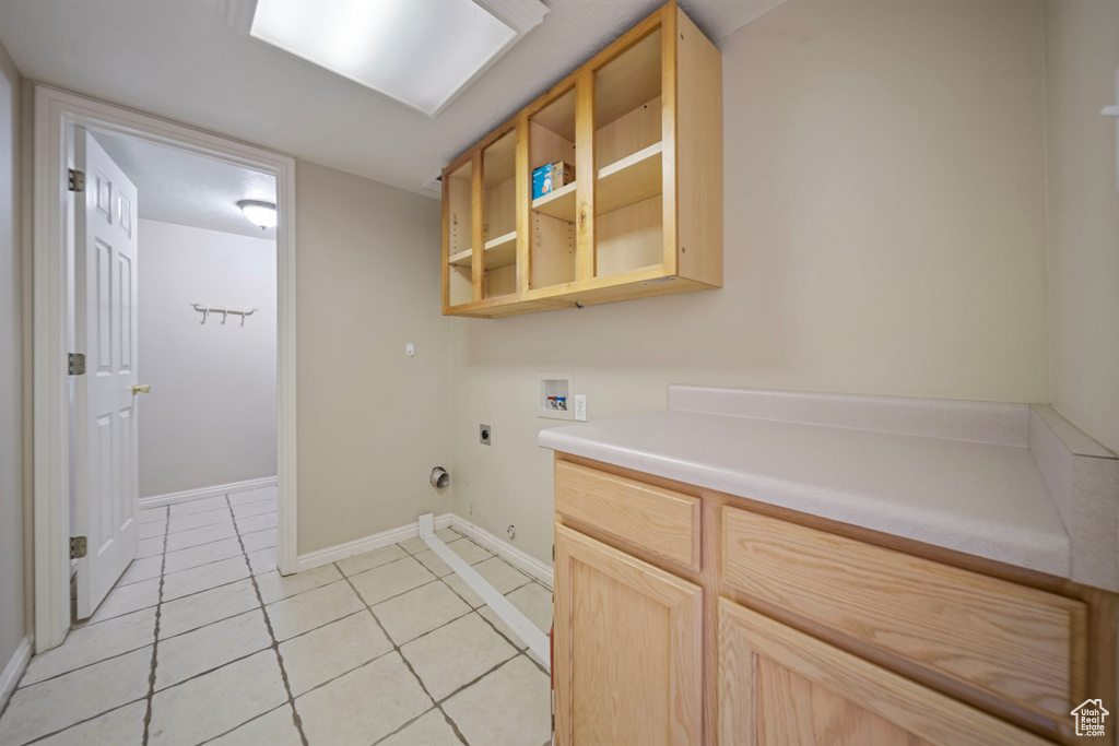 Washroom with cabinet space, light tile patterned flooring, hookup for a washing machine, baseboards, and hookup for an electric dryer