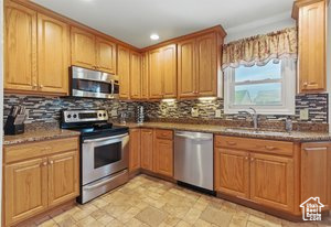 Kitchen with stainless steel appliances, backsplash, recessed lighting, light stone finish floors, and a sink