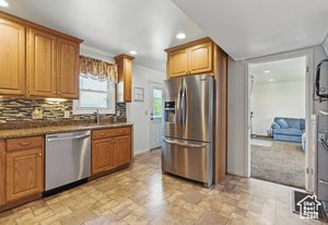 Kitchen with appliances with stainless steel finishes, light stone finish flooring, recessed lighting, tasteful backsplash, and brown cabinetry