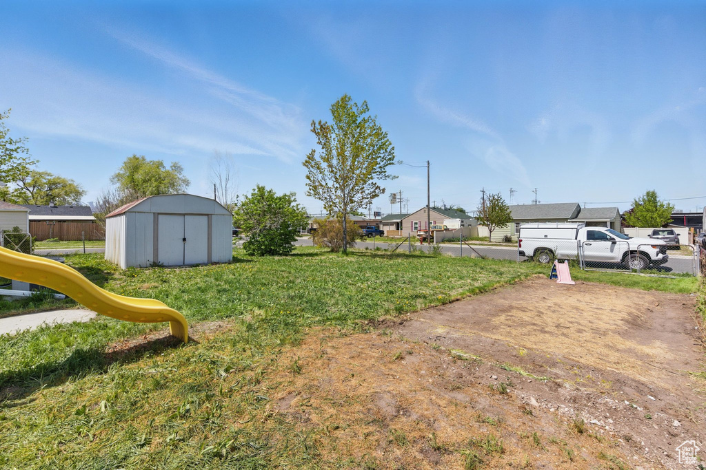 View of yard with an outdoor structure, a shed, a playground, and a residential view