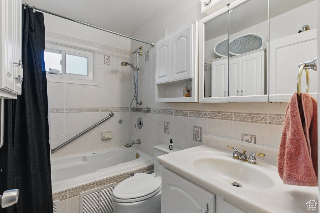 Full bath featuring visible vents, toilet, tiled shower / bath, tile walls, and vanity