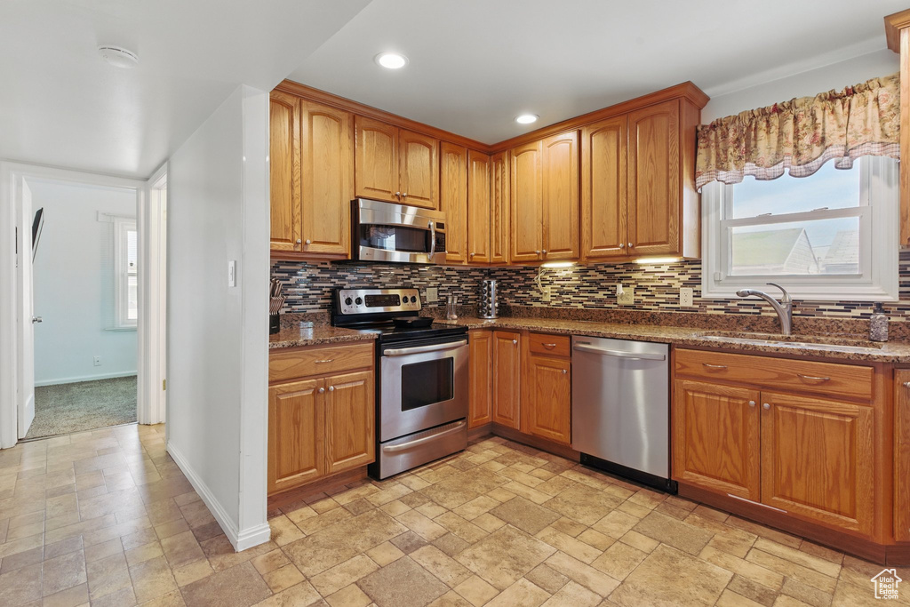 Kitchen featuring a sink, stone tile flooring, tasteful backsplash, baseboards, and appliances with stainless steel finishes