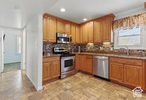 Kitchen with appliances with stainless steel finishes, a sink, decorative backsplash, recessed lighting, and light stone finish floors