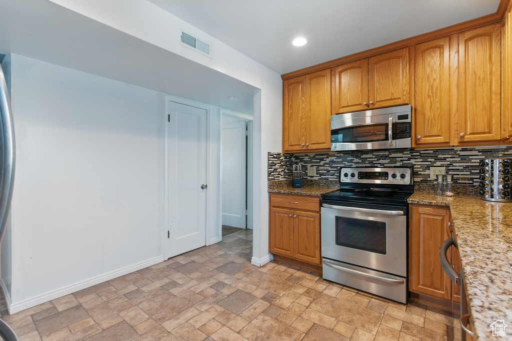 Kitchen featuring appliances with stainless steel finishes, stone finish flooring, visible vents, baseboards, and backsplash