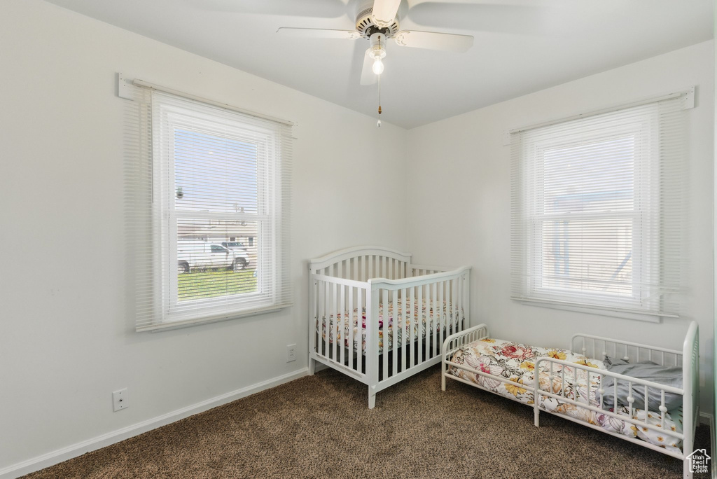 Bedroom featuring baseboards, a nursery area, a ceiling fan, and carpet