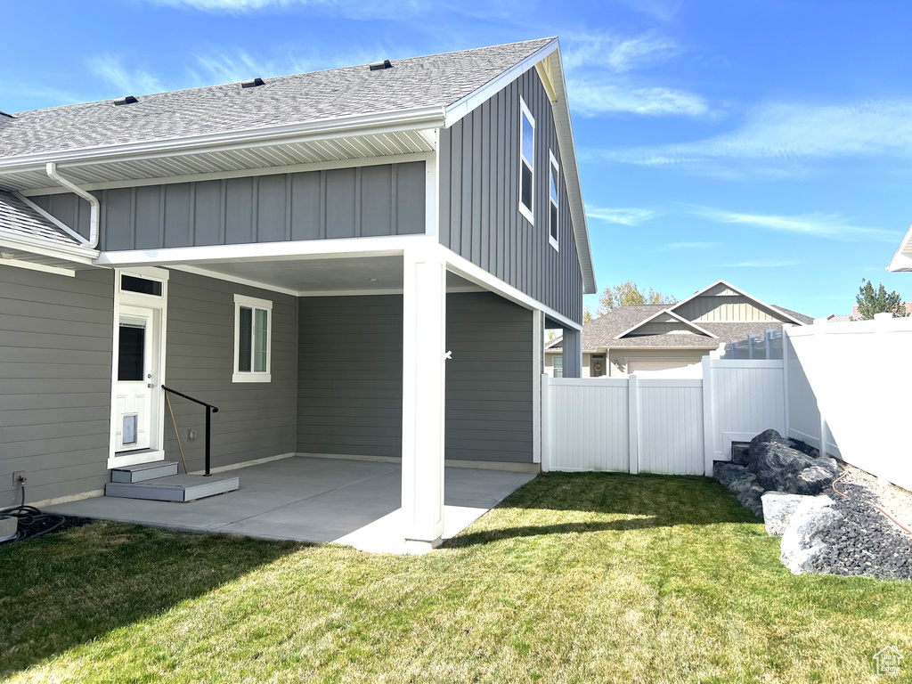 Back of house with a lawn, roof with shingles, fence, and a patio