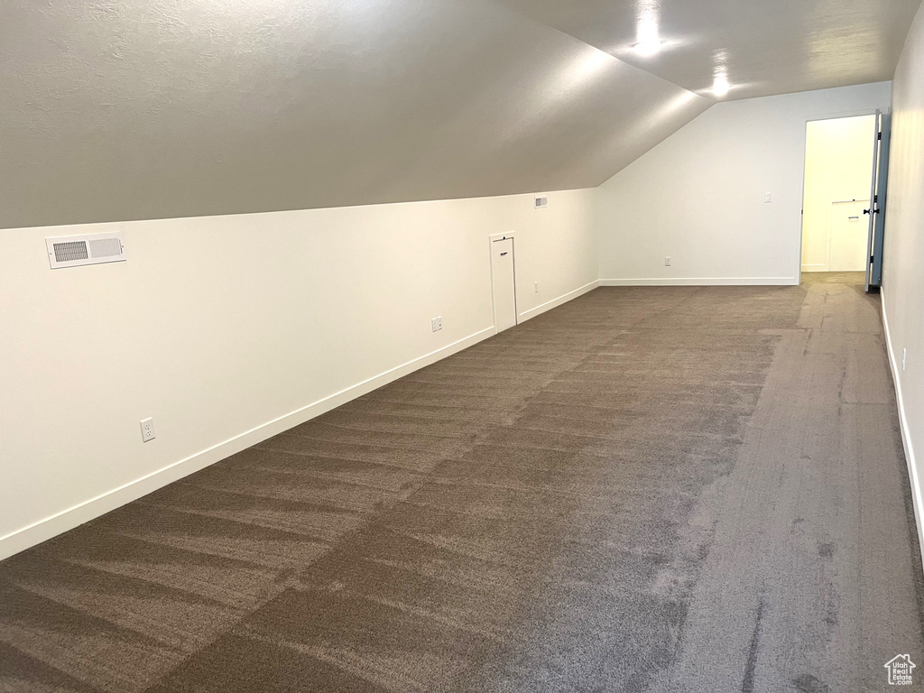 Bonus room with visible vents, baseboards, lofted ceiling, and dark colored carpet
