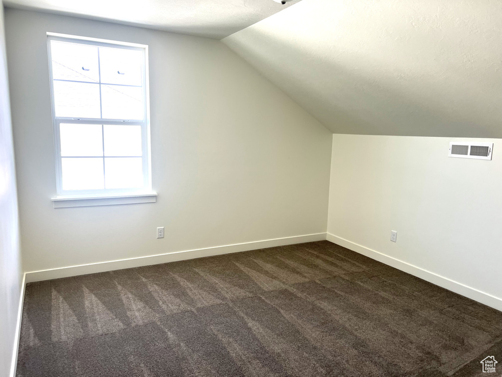 Additional living space with visible vents, baseboards, lofted ceiling, and dark colored carpet