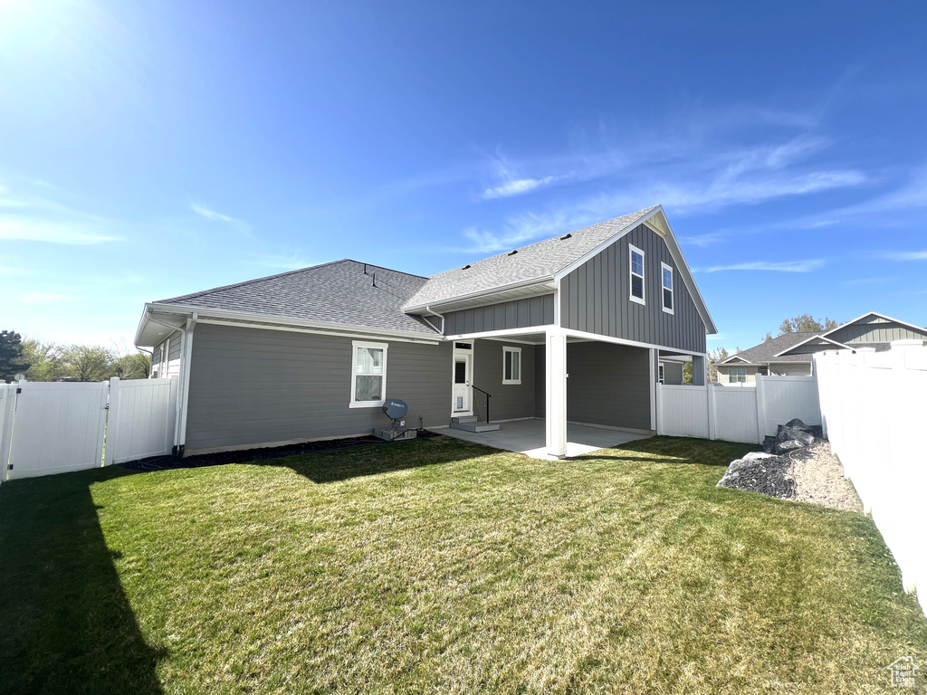 Rear view of house featuring a patio, a fenced backyard, roof with shingles, board and batten siding, and a yard