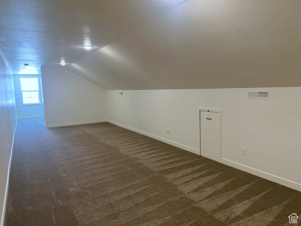 Additional living space featuring baseboards, visible vents, and dark carpet