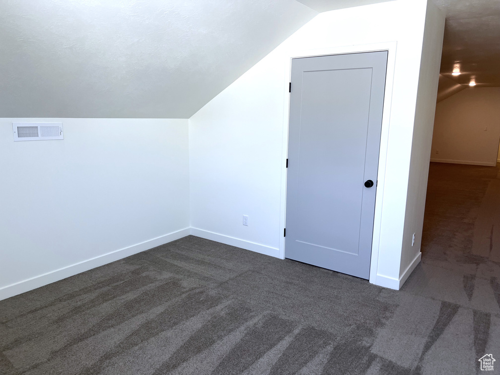 Additional living space featuring baseboards, visible vents, dark colored carpet, and lofted ceiling