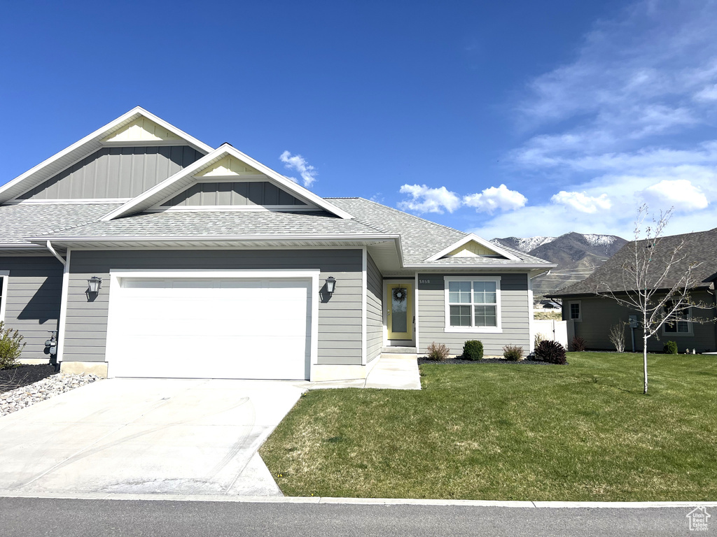 View of front of home with board and batten siding, driveway, a front yard, a garage, and a mountain view